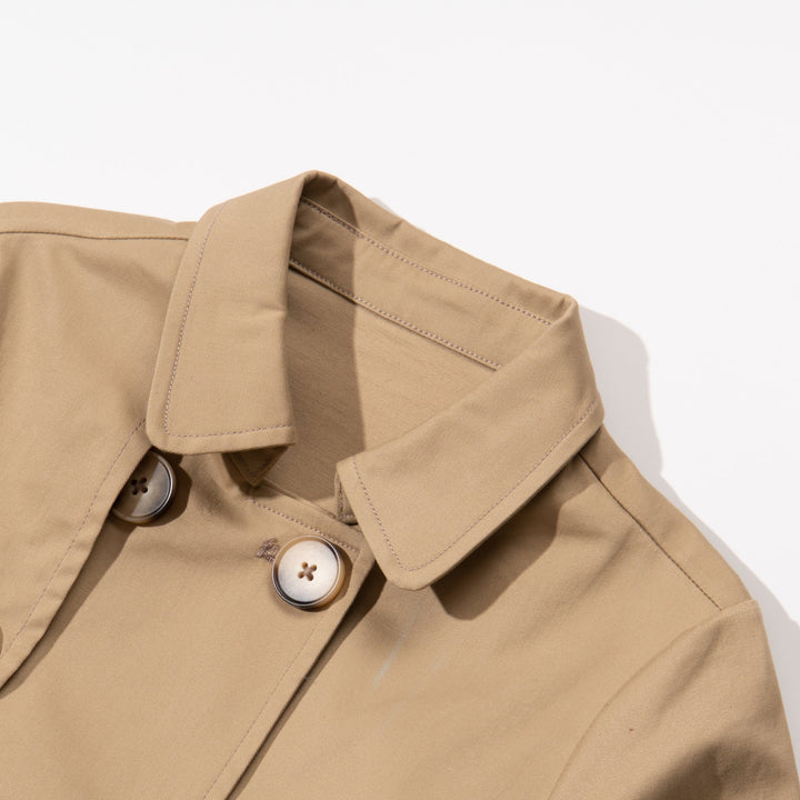 A trench coat, with a pink tutu sewn at the back. Two pockets are at the front and a buttoned panel on the upper left corner. Fastened from the front with faded dark/light brown coat buttons. 