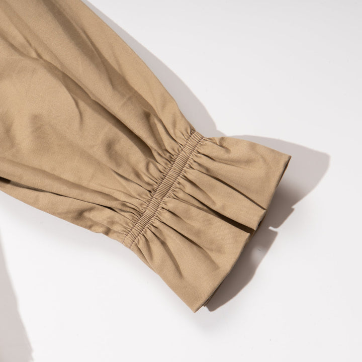 A trench coat, with a pink tutu sewn at the back. Two pockets are at the front and a buttoned panel on the upper left corner. Fastened from the front with faded dark/light brown coat buttons. 