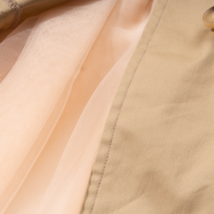 A trench coat, with a pink tutu sewn at the back. Two pockets are at the front and a buttoned panel on the upper left corner. Fastened from the front with faded dark/light brown coat buttons. 