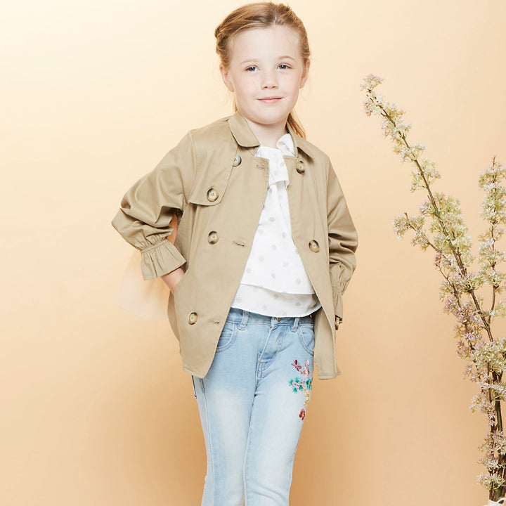 A trench coat, with a pink tutu sewn at the back. Two pockets are at the front and a buttoned panel on the upper left corner. Fastened from the front with faded dark/light brown coat buttons. 