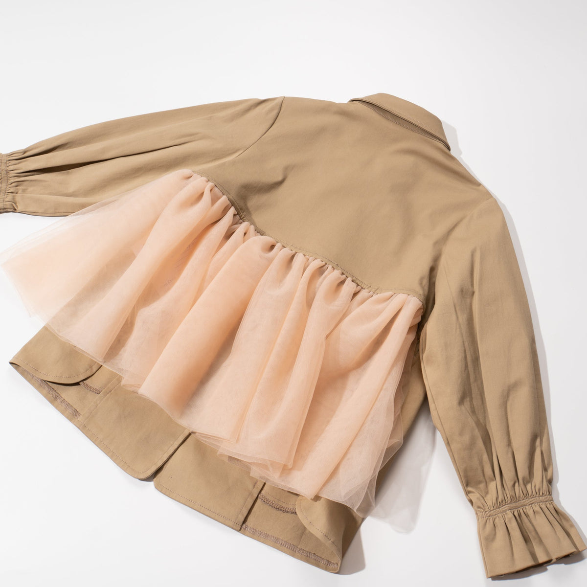 A trench coat, with a pink tutu sewn at the back. Two pockets are at the front and a buttoned panel on the upper left corner. Fastened from the front with faded dark/light brown coat buttons. 