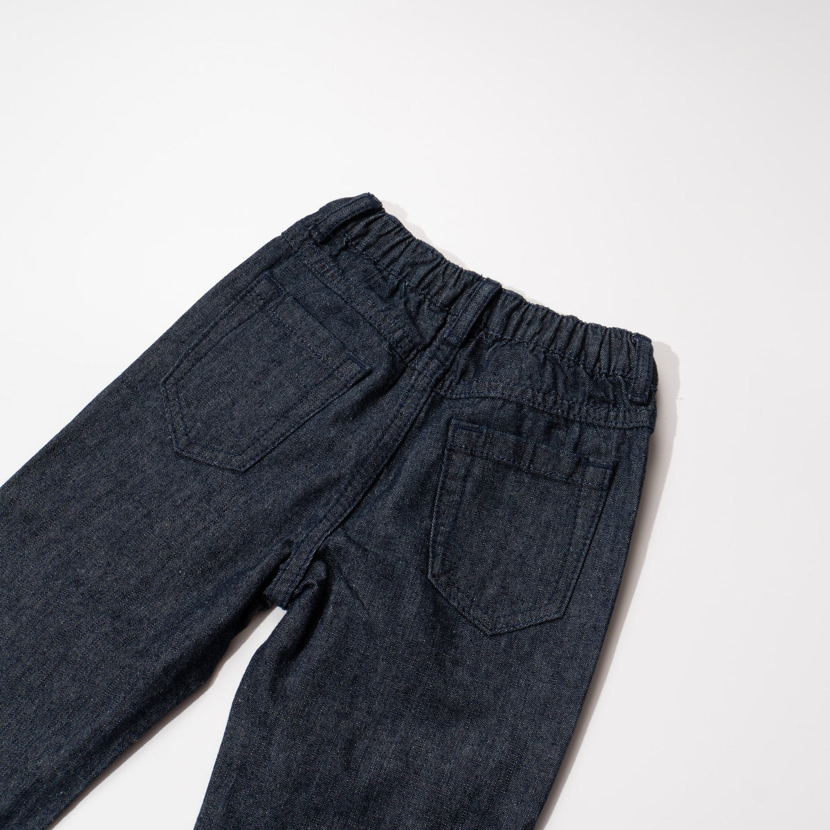 Elasticated dark blue jeans, skeletal dinosaur embroidered one leg front. Embossed caption on other leg front, metallic button fastening.