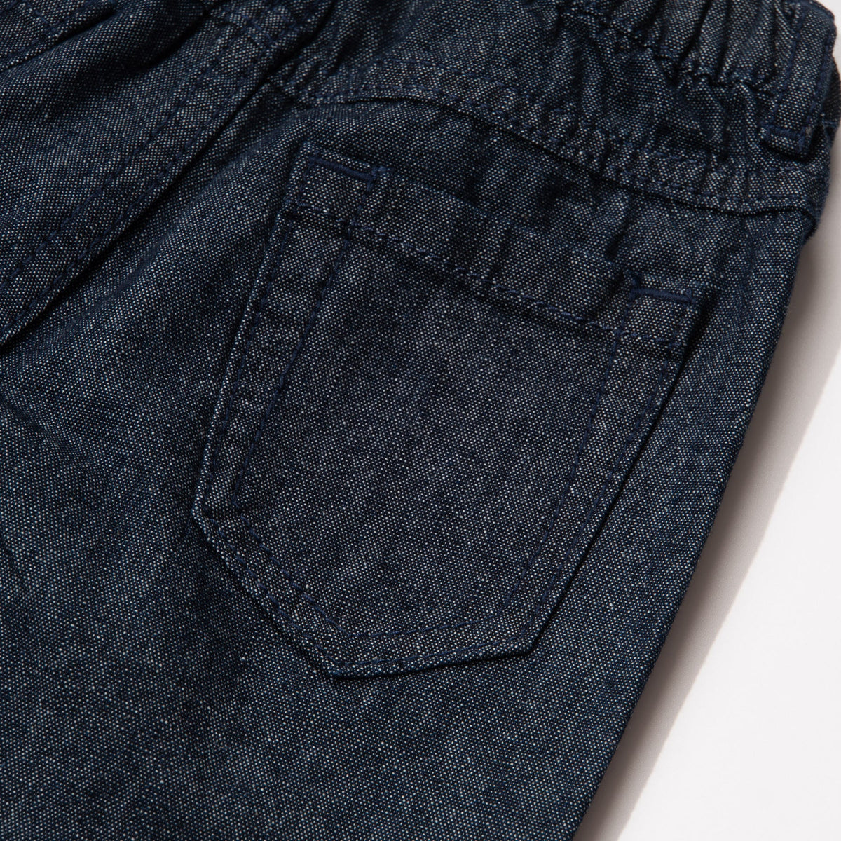 Elasticated dark blue jeans, skeletal dinosaur embroidered one leg front. Embossed caption on other leg front, metallic button fastening.