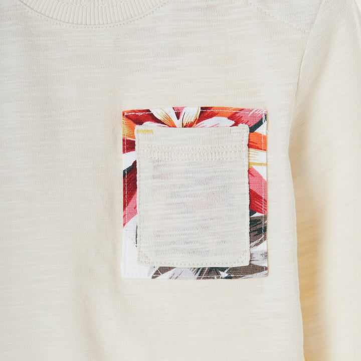 Cream colored, long sleeve top, hidden floral strap visible at the nape, front pocket and backside hem. 