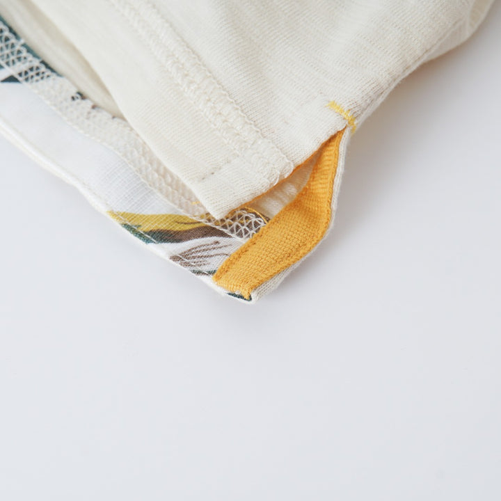 Cream colored, long sleeve top, hidden floral strap visible at the nape, front pocket and backside hem. 