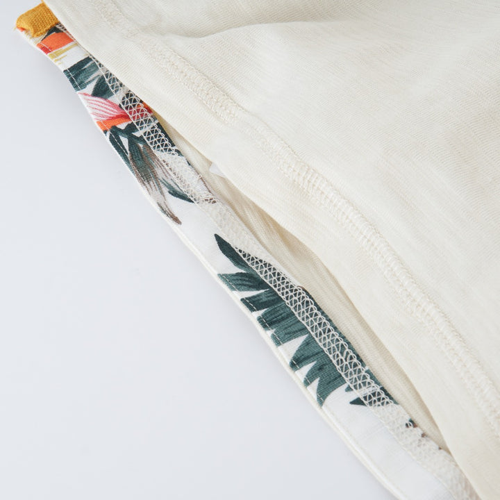 Cream colored, long sleeve top, hidden floral strap visible at the nape, front pocket and backside hem. 