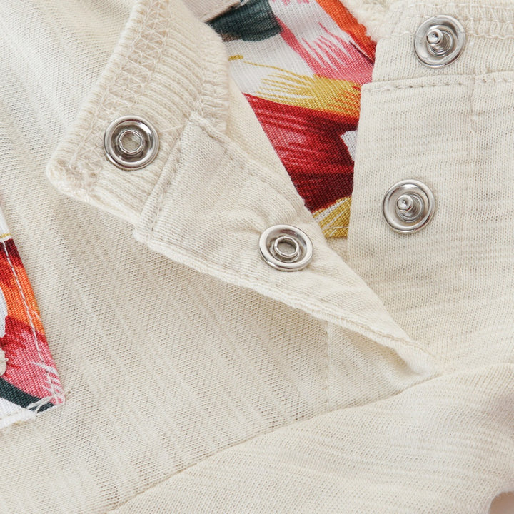Cream colored, long sleeve top, hidden floral strap visible at the nape, front pocket and backside hem. 