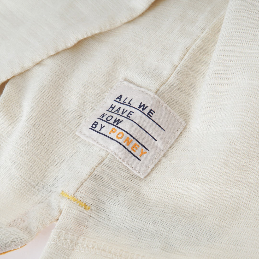 Cream colored, long sleeve top, hidden floral strap visible at the nape, front pocket and backside hem. 