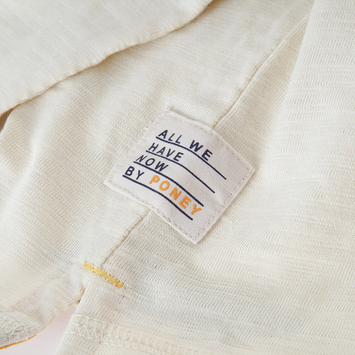 Cream colored, long sleeve top, hidden floral strap visible at the nape, front pocket and backside hem. 