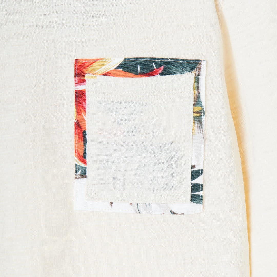 Cream colored, long sleeve top, hidden floral strap visible at the nape, front pocket and backside hem. 