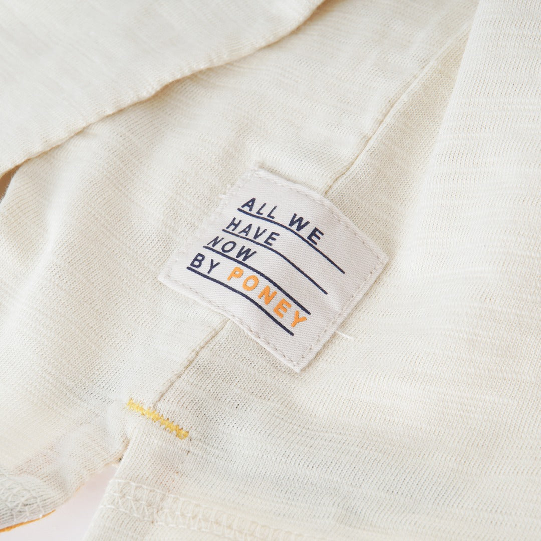 Cream colored, long sleeve top, hidden floral strap visible at the nape, front pocket and backside hem. 
